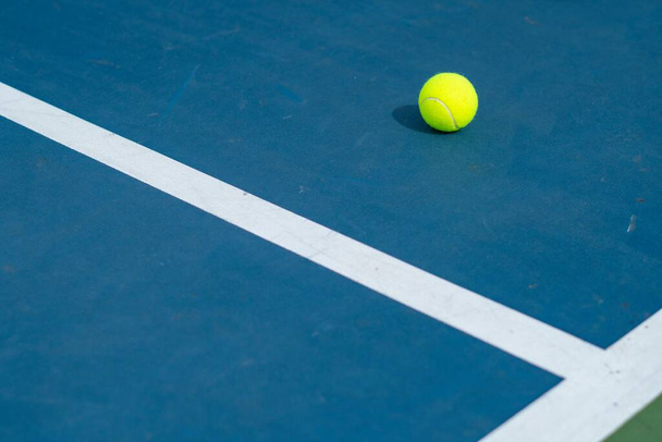 A landscape of a blue and green tennis court with a ball on it on a sunny day - Фото, зображення
