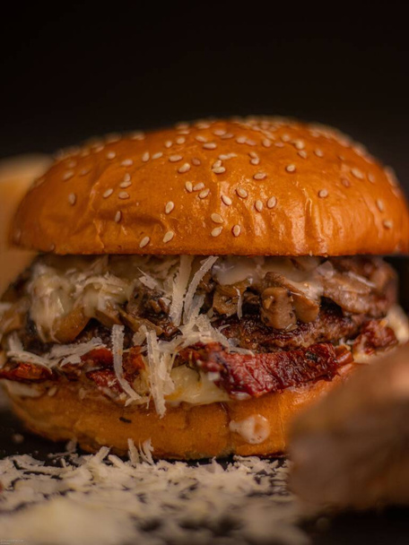A vertical shot of a burger with parmesan cheese on a dark background. - Фото, изображение