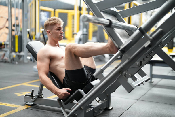Молодой активный спортсмен, тренирующийся на тренажерах в фитнес-центре или тренажерном зале - Фото, изображение