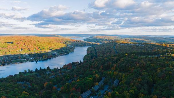 An aerial of a scenic lake surrounded by a dense forest with autumn foliage in fall colors - Fotografie, Obrázek