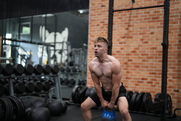 Молодой активный спортсмен, тренирующийся на тренажерах в фитнес-центре или тренажерном зале - Фото, изображение