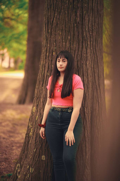 A vertical shot of a beautiful young woman standing behind a tree in a forest - 写真・画像