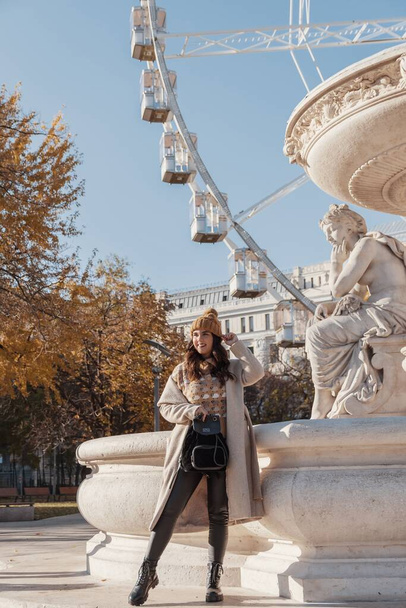 A vertical image of an attractive woman posing in front of Budapest eye ferris wheel during autumn in Budapest, Hungary - Φωτογραφία, εικόνα