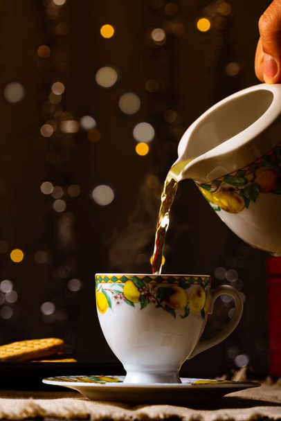 A beautiful shot of tea being poured from a jug into a cup with lemons on a table - Fotó, kép