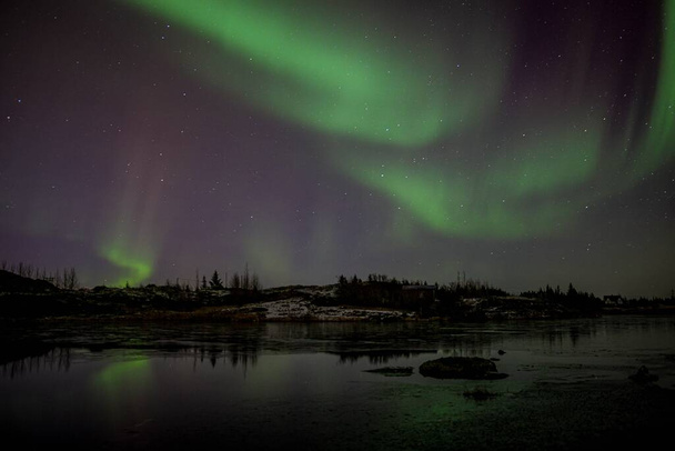 A scenic shot of an Aurora Borealis reflecting on a lake in Iceland during nighttime - 写真・画像