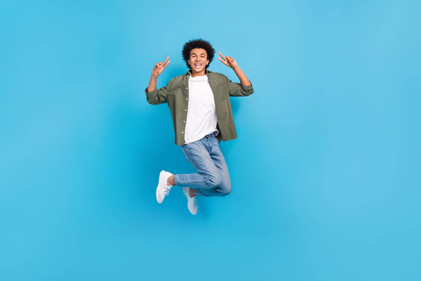 Full body cadre of young jumping carefree active man show double v-sign wear trendy look shopping advert isolated on blue color background. - Photo, image