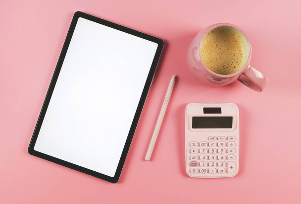 Top view or flat lay of digital tablet with blank white screen, pink stylus pen,  pink cup of coffee,  and pink  calculator  isolated on pink background. - Foto, Imagen