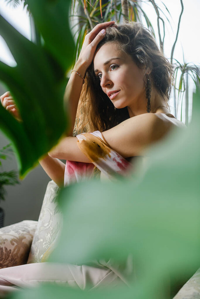 Portrait de femme sensuelle assise entre les plantes de la maison, feuilles vertes fraîches, chambre confortable avec lumière naturelle - Photo, image