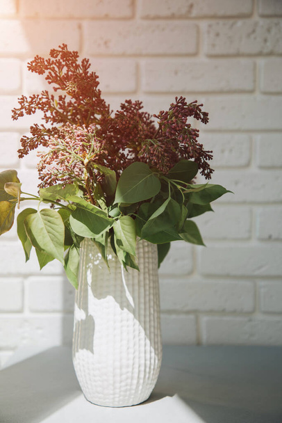 A bouquet of lilacs in a white vase on a white brick wall with a shadow. Front view - Photo, Image