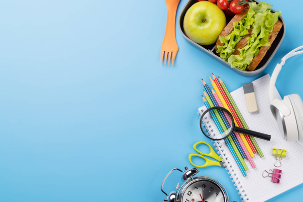 School supplies, stationery, and lunch box on blue background. Education and nutrition. Flat lay with blank space - Foto, afbeelding