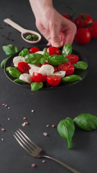 Caprese salade met rijpe tomaten en mozzarella kaas met verse basilicum bladeren op zwarte achtergrond. Italiaans eten. Verticale video - Video