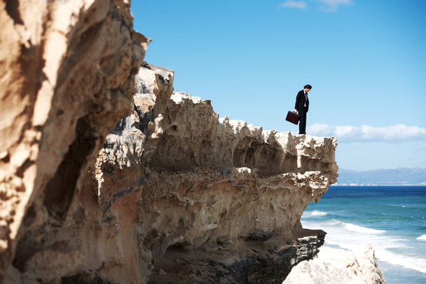 Its a long way down...Businessman holding a briefcase standing on a cliff looking down towards the ocean - Φωτογραφία, εικόνα