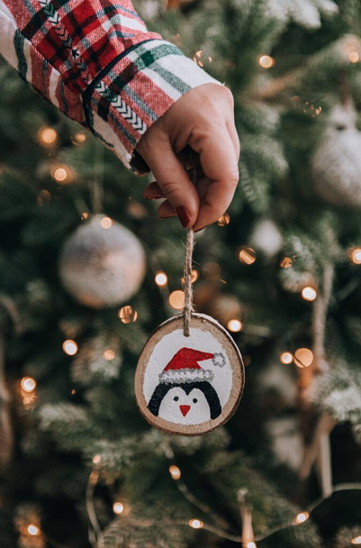Close-up photo of woman wearing plaid pyjamas, holding diy christmas ornament in front of christmas tree. - Фото, зображення