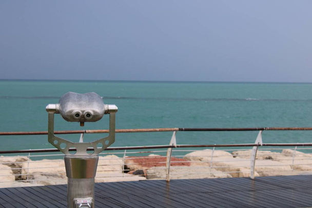An outdoor telescope on a wooden dock protected with railings, overlooking the beautiful seascape - Photo, image