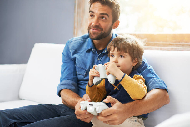 Gry wideo, ojciec i syn na kanapie, gry i więzi dla jakości czasu, domu i relaksu. Rodzina, szczęśliwy tata i chłopiec z rodzicem, mężczyzna dziecko i dziecko z kontrolerem, szczęście i rozrywka. - Zdjęcie, obraz