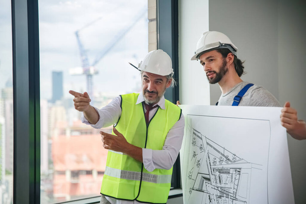 Чоловіки-інженери, що стоять на будівельному майданчику, тримають креслення
. - Фото, зображення