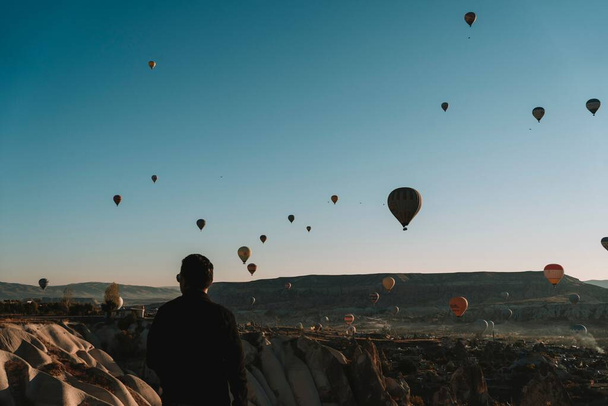 Een man kijkend naar vliegende Hete Lucht ballon in de blauwe lucht in Cappadocia, Turkije - Foto, afbeelding