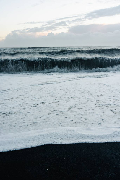 A vertical shot of the sea waves and foam against the background of the cloudy sky. - Foto, imagen