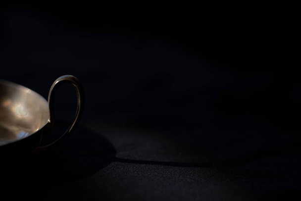 A closeup shot of the handle of a silver bowl and its shadow on a black background - Valokuva, kuva