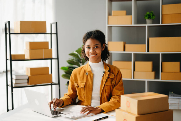 Small business entrepreneur SME freelance African woman working at home office and laptop online, marketing, packaging, delivery,  e-commerce concept - Foto, imagen