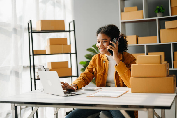 Small business entrepreneur SME freelance African woman working at home office and laptop online, marketing, packaging, delivery,  e-commerce concept - 写真・画像