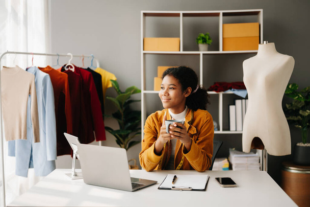 Calm curly brunette, dark skinned woman on desk in modern office of fashion designer and  laptop and smartphone. - Φωτογραφία, εικόνα