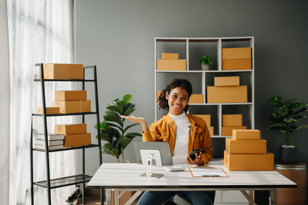 Small business entrepreneur SME freelance African woman working at home office, tablet and phone online, marketing, packaging, delivery,  e-commerce concept - 写真・画像