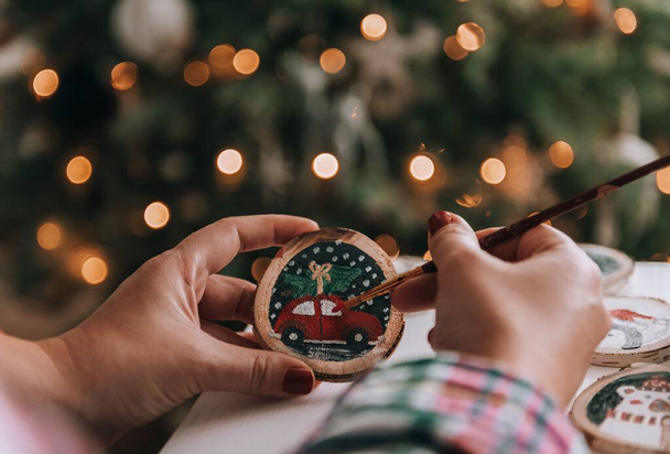 Close-up photo of woman crafting christmas ornaments, painting on a slice of wood. - Foto, Imagen