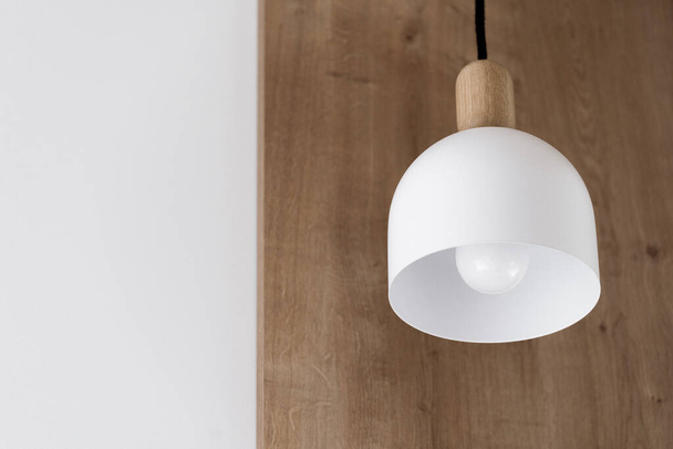 closeup of white ceiling lamp hanging on wooden background in room with stylish interior. decorative light equipment in contemporary apartment - Foto, imagen