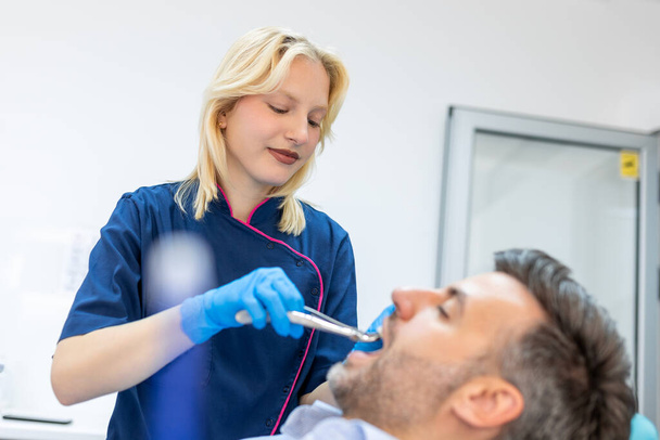 Treatment of a patient with a dentist surgeon. Extraction of teeth and prosthetics. Doctor performing extraction procedure with forceps removing patient tooth. Healthcare dentistry medicine concept - Photo, Image