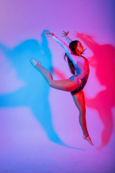Гнучка дівчинка, ритмічний гімнастичний художник стрибає на білому темному фоні. Ґрейс в русі, дії. - Фото, зображення