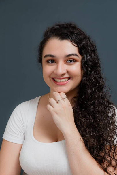 Young smiling woman looking at camera with hand on chin. Against gray background. - Foto, immagini