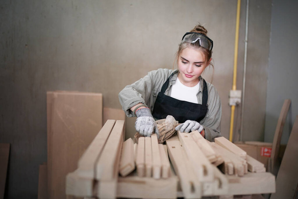 Jonge mooie vrouw doet werk in de timmerman doe-het-zelf werkplaats. Kleine ondernemer, jonge vrouw die in de meubelfabriek werkt. - Foto, afbeelding