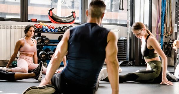 Сильні спортсмени в активному одязі тренуються разом і розтягують ноги, сидячи на підлозі спортзалу під час тренувань
 - Фото, зображення
