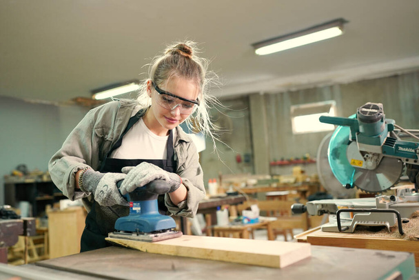 Молодая красивая женщина, работающая в мастерской плотника. Владелец малого бизнеса, молодая женщина, работающая на мебельной фабрике. - Фото, изображение