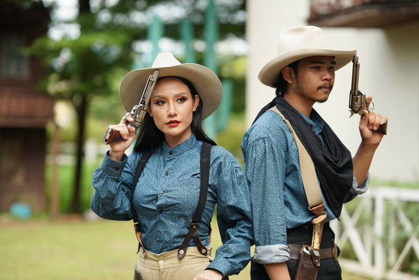 Brutální kovboj a kovbojka s revolvery na ranči. Lidé se zbraněmi, divoký západní životní styl - Fotografie, Obrázek