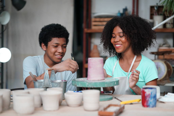 Νεαρή Αφρο κορίτσι και αγόρι αγγειοπλάστη κατασκευή πήλινου αγγείου σε εργαστήριο κεραμικής, ιδιοκτήτης επιχείρησης.  - Φωτογραφία, εικόνα