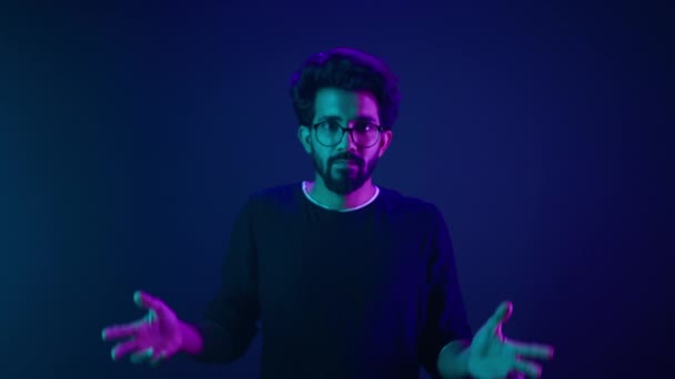 Studio dark blue neon background Indian man Arabian male model guy confused shrug shoulders unsure doubtful shrugging doubt uncertain dont know problem solution question guess puzzled bemused no clue - Footage, Video