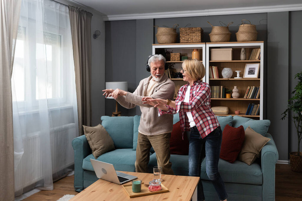 Joyful active old retired romantic couple dancing laughing in living room, happy middle aged wife and elder husband having fun at home, smiling senior family grandparents relaxing bonding together - Foto, Imagen