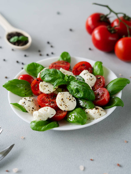 Итальянский салат капрезе с нарезанными помидорами, сыром моцарелла, базиликом, оливковым маслом на светлом фоне. Вегетарианская еда - Фото, изображение