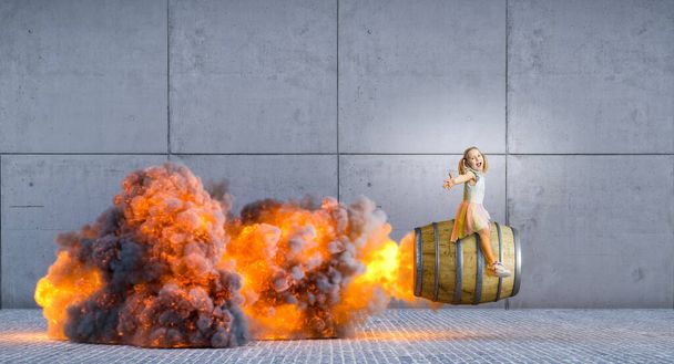 Happy little girl rides a large wooden barrel with propulsion, flames and smoke from behind - Foto, Imagen