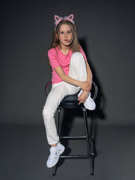A cheerful but serious teenage girl with long, blond hair in a pink T-shirt and jeans posing in the studio. On a gray background. Freedom concept - Foto, Imagen