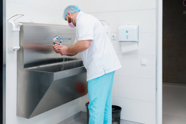Desinfektionsverfahren in der Klinik: Der Chirurg wäscht sich vor der Operation die Hände im Waschbecken - Foto, Bild