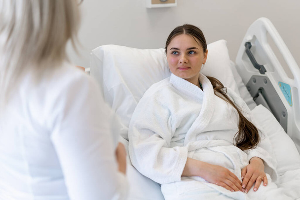 eine Ärztin, die in einem Krankenhauszimmer am Bett steht und mit einer jungen Patientin einen Behandlungsplan diskutiert - Foto, Bild