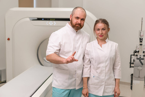 Улыбающиеся и довольные врачи в униформе позируют рядом с магнитно-резонансной томографией концепция машины профессий и медицины - Фото, изображение
