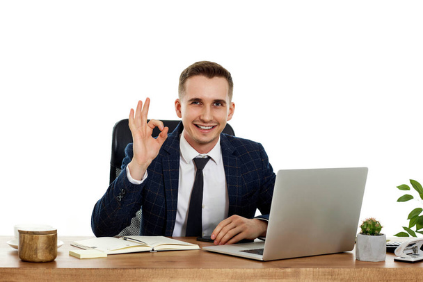 fiatal boldog üzletember ül az asztalnál dolgozik laptop PC számítógép és bemutatja Ok gesztus - Fotó, kép