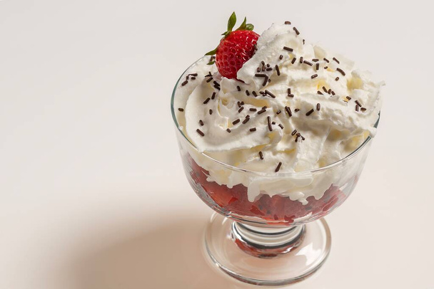 Leckeres Dessertglas mit Erdbeeren, Sahne und Schokoladenstücken auf weißem Hintergrund. Horizontales Foto und selektiver Fokus - Foto, Bild