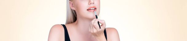Closeup personable young woman with flawless healthy skin and natural makeup putting fashion glossy lipstick on her lip with lip brush in isolated background. Facial cosmetic makeup in process. - 写真・画像