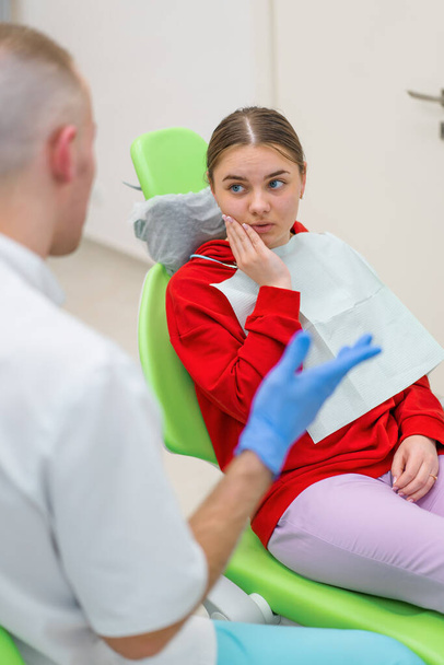 Dişçi randevusundaki üzgün kadın hasta diş ağrısı ve dişçi muayenehanesini tutmaktan şikayetçi. - Fotoğraf, Görsel