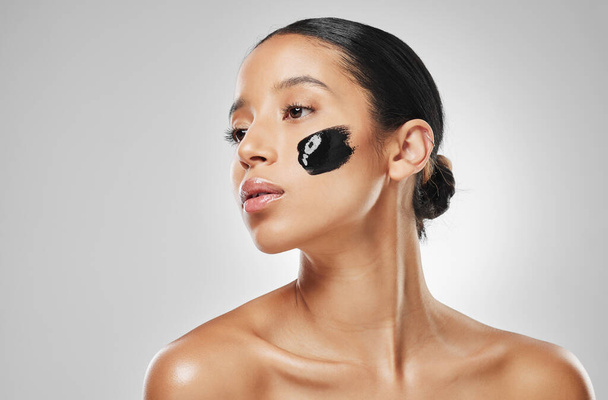 It takes minutes to get a purified complexion. Studio shot of an attractive young woman wearing some charcoal face mask against a grey background - Fotó, kép